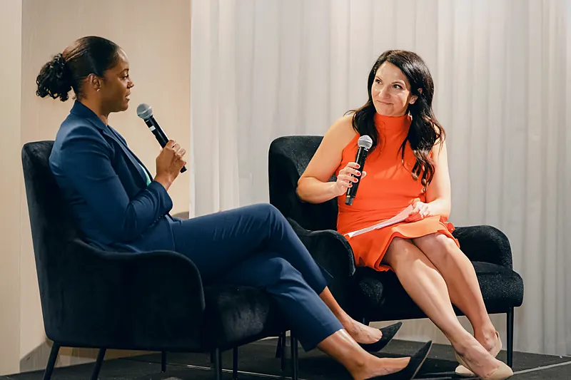 Me on stage in an orange dress, smiling as I listen to the woman I'm interviewing